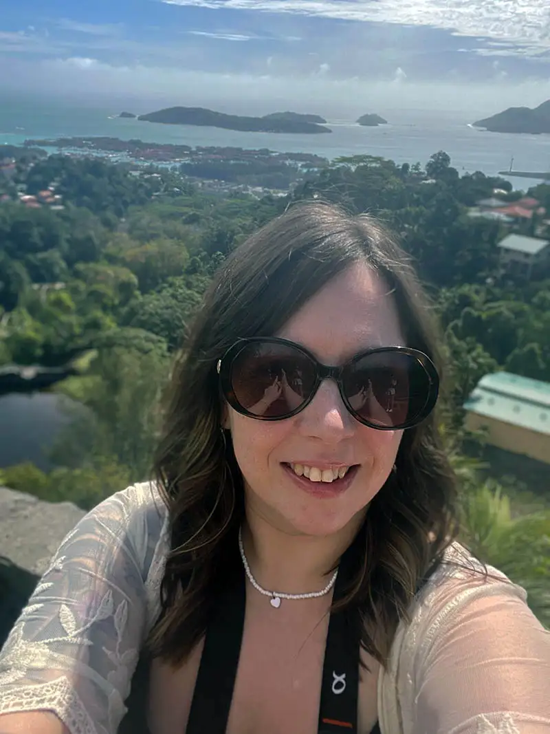 Selfie of Scottish artist Michelle Tierney standing on a mountainside in the Seychelles with panoramic ocean views and tropical coastline in the background.